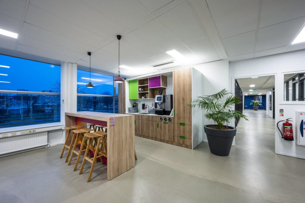 Moderne kantoorkeuken met een zithoek, koffieautomaat, planten en uitzicht op de Van der Madeweg.